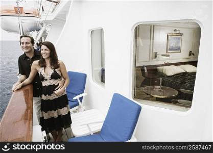 Mid adult couple standing at the railing of a sailing ship and smiling