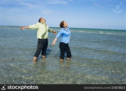 Mid adult couple standing on the beach with their arms outstretched