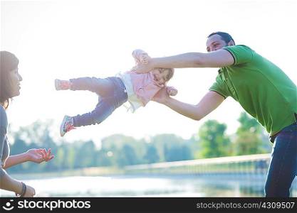 Mid adult couple swinging toddler daughter at riverside