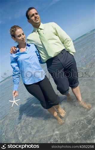 Mid adult couple wading on the beach with their arms around each other