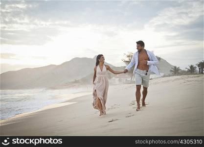 Mid adult couple walking along beach, hand in hand