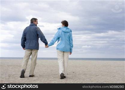 Mid-adult couple walking hand in hand on the beach