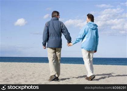 Mid-adult couple walking hand in hand on the beach