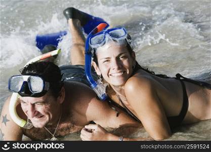 Mid adult couple wearing snorkeling gear and lying on the beach