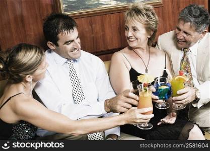 Mid adult couple with a mature woman and a senior man toasting glasses of cocktail