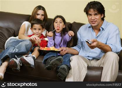 Mid adult couple with their children sitting on a couch and watching television