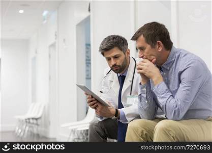Mid adult doctor explaining serious patient over digital tablet at hospital