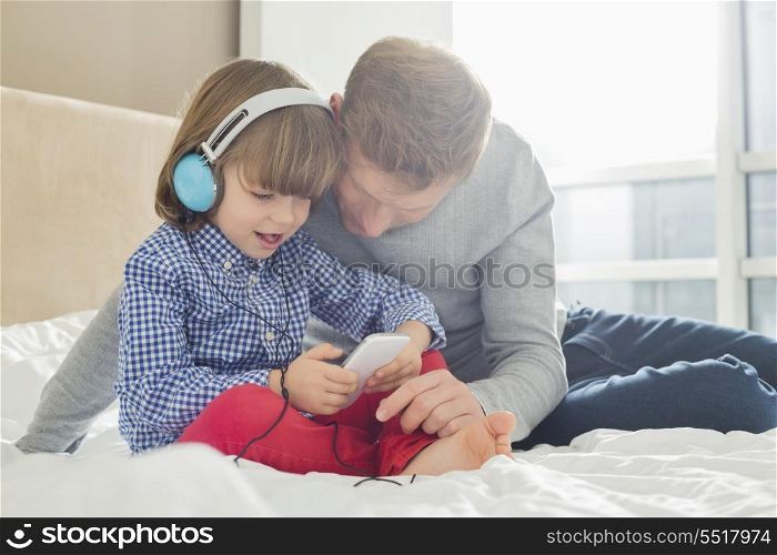 Mid adult father with boy listening music on headphones in bedroom