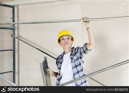 Mid adult female architect looking up while standing under scaffold at construction site
