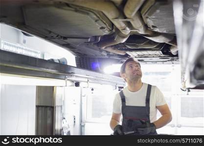 Mid adult male automobile mechanic worker examining car in workshop