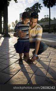 Mid adult man adjusting his son&acute;s sandals, Malecon, Santo Domingo, Dominican Republic
