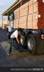 Mid-adult man adjusting strapping of truck loaded with wood