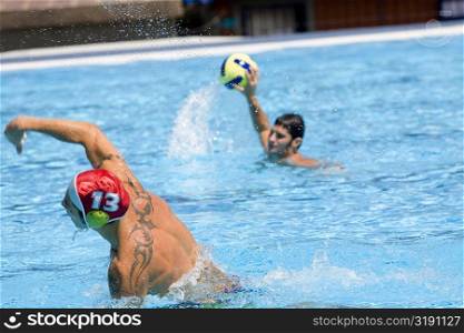 Mid adult man and a young man playing water polo in a swimming pool