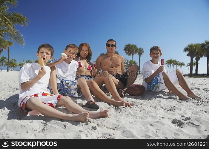 Mid adult man and a young man sitting with their children on the beach