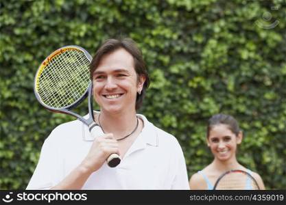 Mid adult man and a young woman holding tennis rackets and smiling