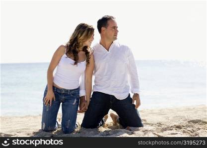 Mid adult man and a young woman kneeling with holding hands on the beach