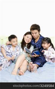 Mid adult man and a young woman reading a book on the bed with their children