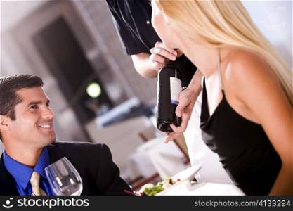 Mid adult man and a young woman sitting at a table with a waiter standing beside them