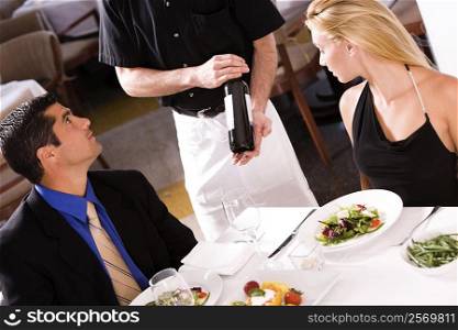Mid adult man and a young woman sitting at the table with a waiter showing them a wine bottle
