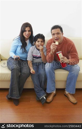 Mid adult man and a young woman sitting with their son on a couch and watching television