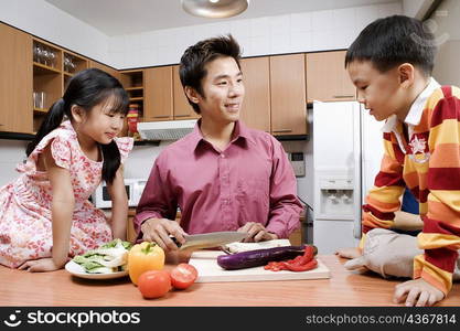 Mid adult man and his children cutting vegetables at a kitchen counter