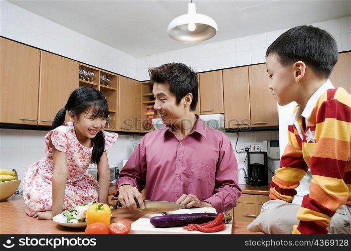 Mid adult man and his children cutting vegetables at a kitchen counter