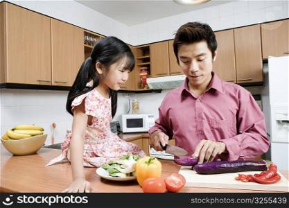 Mid adult man and his daughter cutting vegetables at a kitchen counter