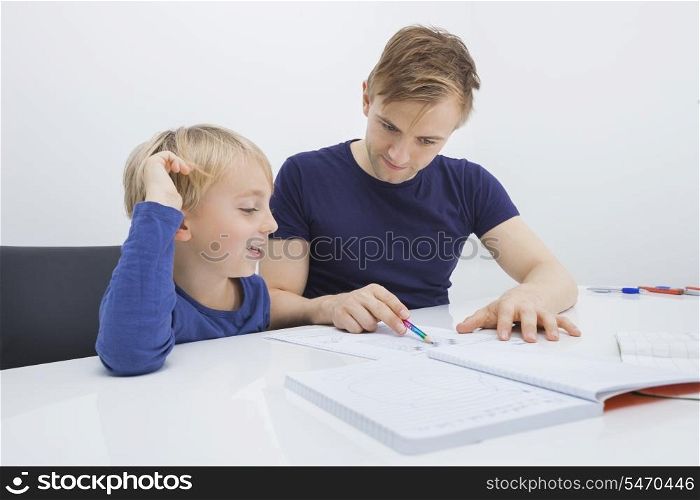 Mid adult man assisting boy in studies at table