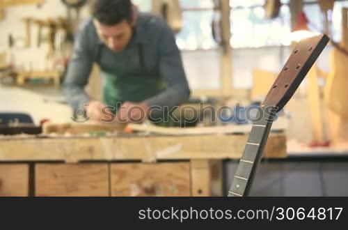 Mid adult man at work as craftsman in workshop with guitars and musical instruments, smoothing guitar body