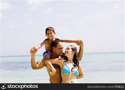 Mid adult man carrying his son on his shoulders with a young woman standing in front of him on the beach
