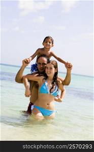 Mid adult man carrying his son on his shoulders with a young woman standing in front of him on the beach