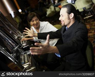 Mid adult man cheering in front of a slot machine with a mature woman smiling beside him