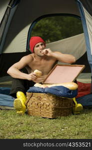 Mid adult man eating a bun sitting in a dome tent