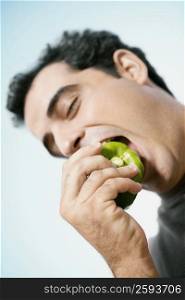 Mid adult man eating a green bell pepper