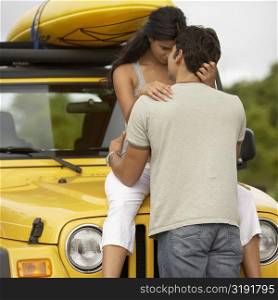 Mid adult man embracing a young woman sitting on the bonnet of a jeep