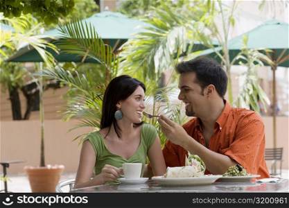 Mid adult man feeding a teenage girl with a fork at a restaurant