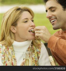 Mid adult man feeding grapes to a young woman