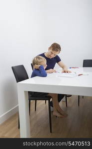 Mid adult man helping boy in studies at table