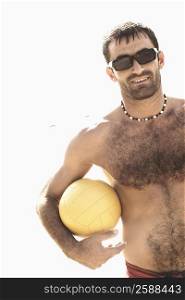 Mid adult man holding a beach volleyball on the beach