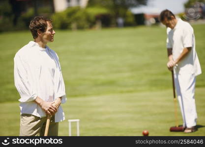 Mid adult man holding a croquet mallet with a mature man standing in the background