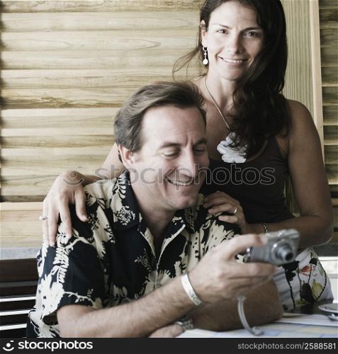 Mid adult man holding a digital camera with a mid adult woman standing beside him
