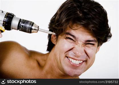 Mid adult man holding a drill machine against his head