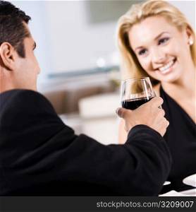 Mid adult man holding a glass of red wine with a young woman sitting beside him