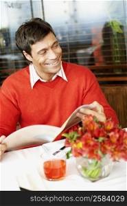 Mid adult man holding a menu in a restaurant and smiling