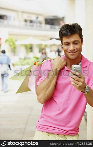 Mid adult man holding a shopping bag and operating a mobile phone