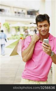 Mid adult man holding a shopping bag and operating a mobile phone