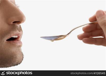 Mid adult man holding a spoon and taking medicine
