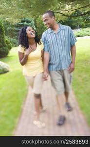 Mid adult man holding hands of a young woman and walking in a lawn