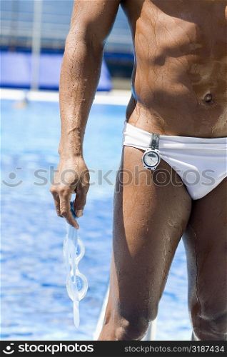 Mid adult man holding swimming goggles and standing at the poolside