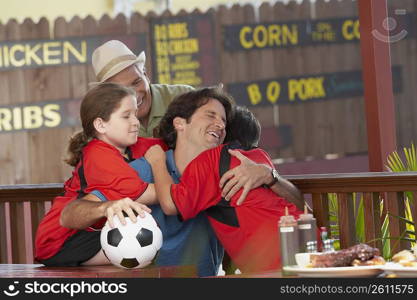 Mid adult man hugging his son in a restaurant with his father and daughter behind him